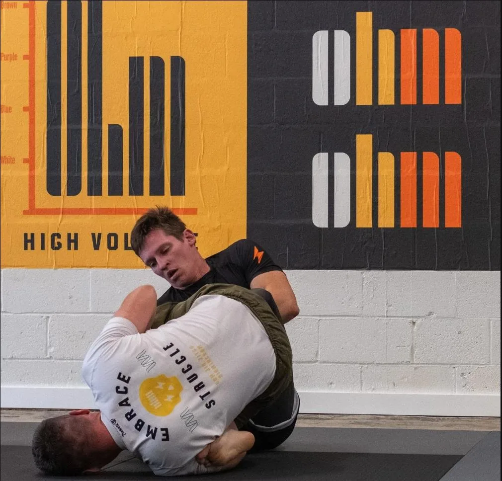 Members training no-gi jiu jitsu at Ohm Jiu Jitsu in Birmingham, branded posters on the wall behind them.
